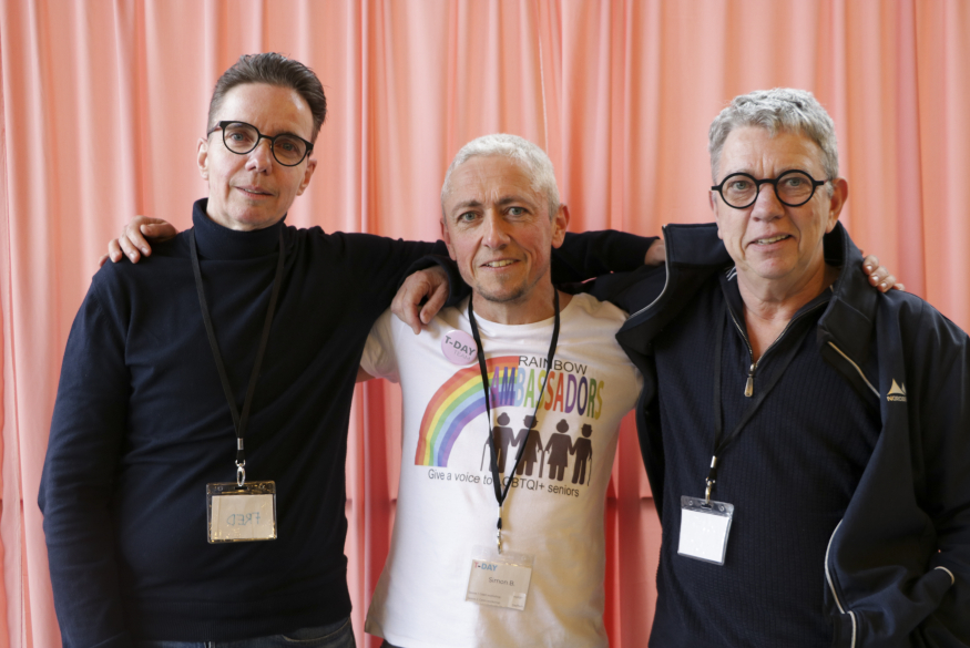 Foto van drie personen voor een roze gordijn