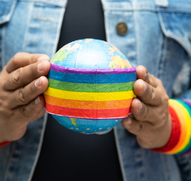persoon die aardbol vastheeft met regenboogband en rond de polsen twee regenboogbanden heeft
