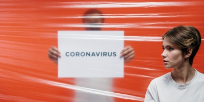 persoon in wit tshirt achter plastiek folie met bord ''coronavirus'