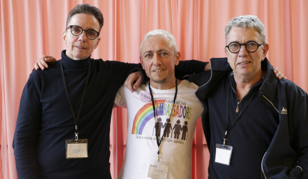 Foto van drie personen voor een roze gordijn