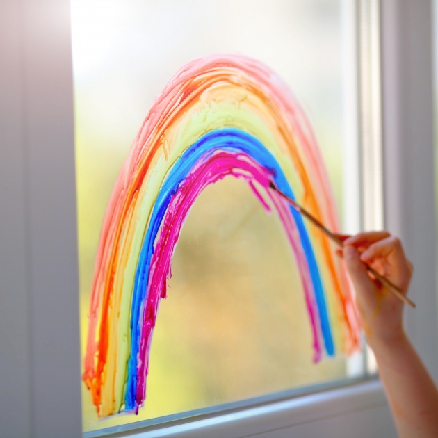 een kind schildert een regenboog op een ruit