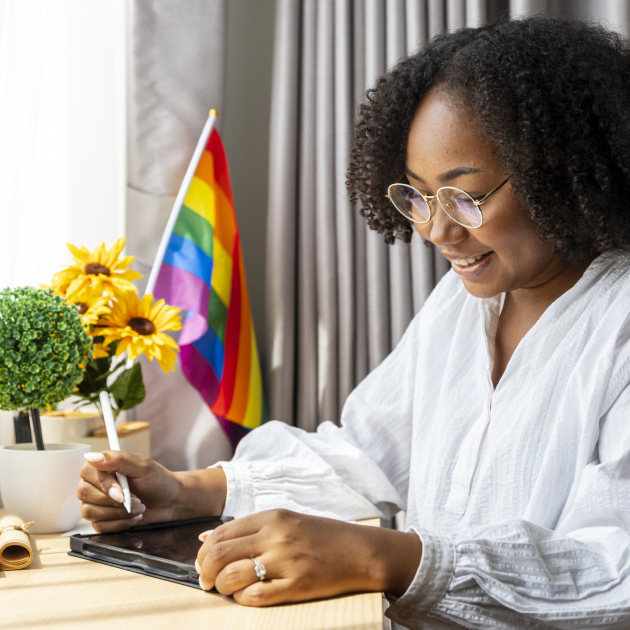LGBTI+ op de werkvloer persoon die aan bureau zit met een regenboogvlagje op de achtergrond
