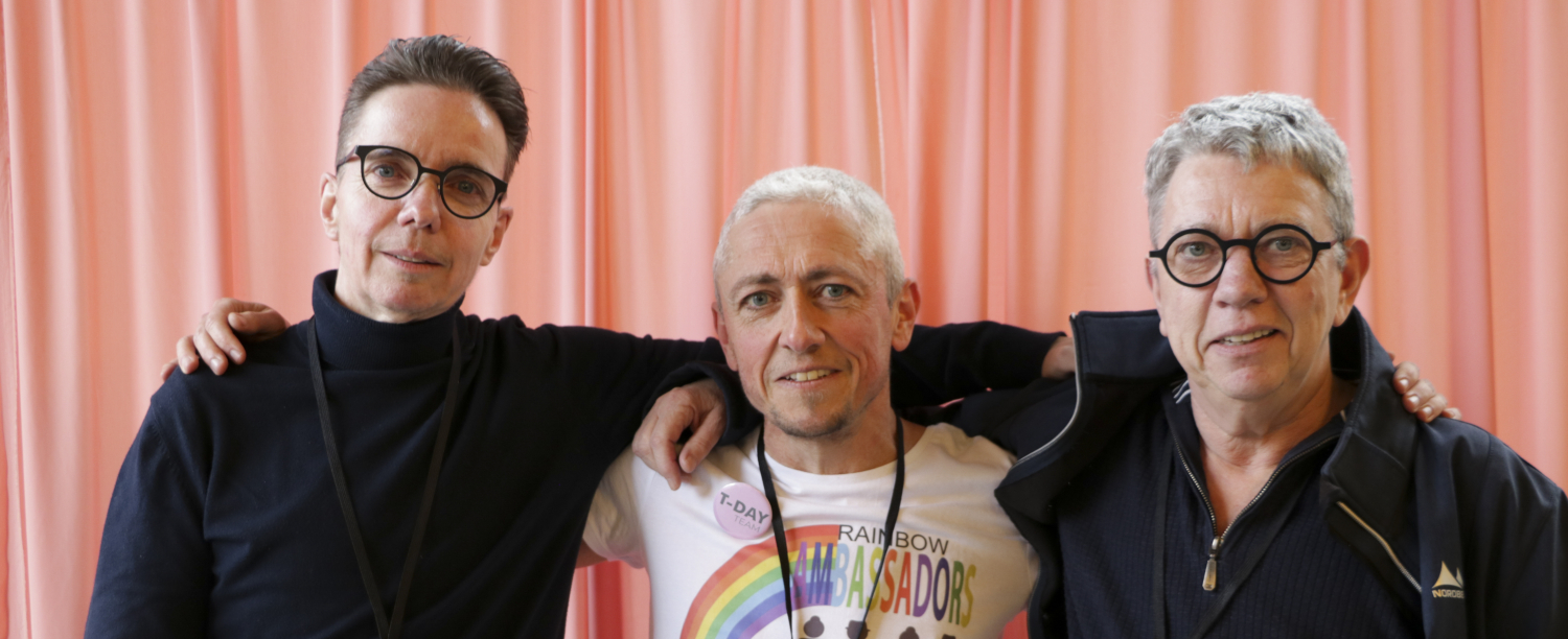 Foto van drie personen voor een roze gordijn