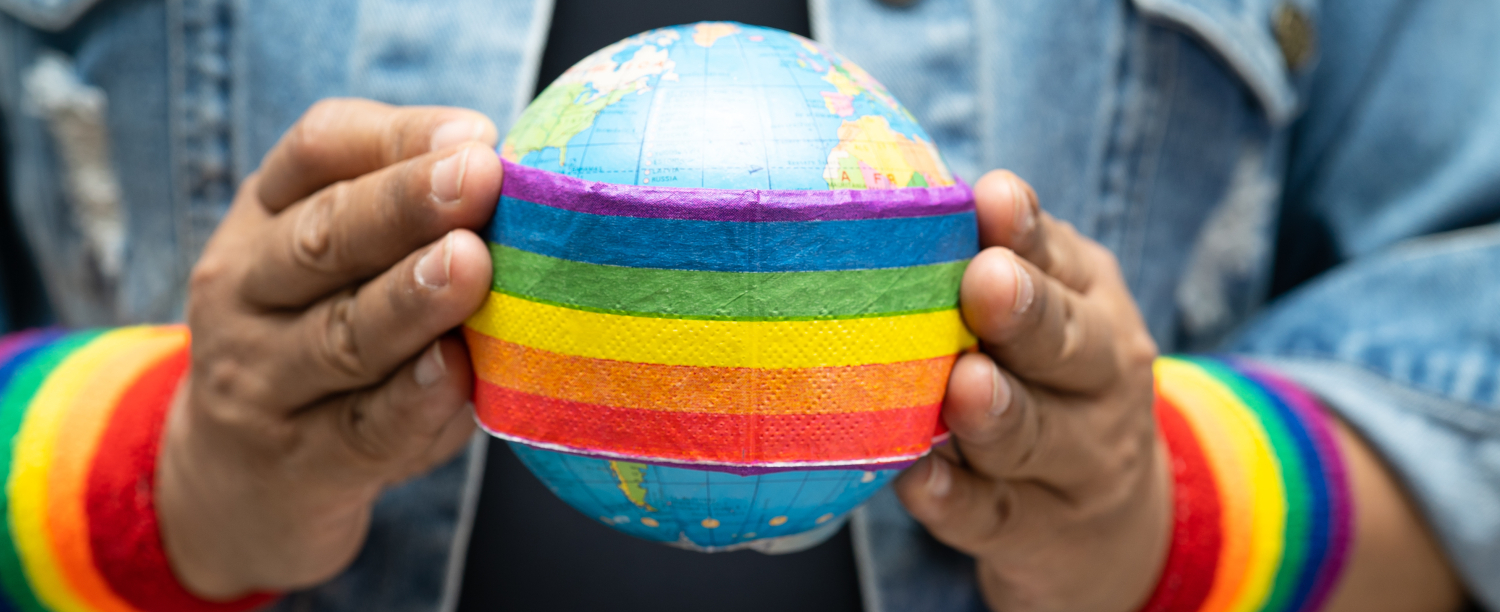 persoon die aardbol vastheeft met regenboogband en rond de polsen twee regenboogbanden heeft