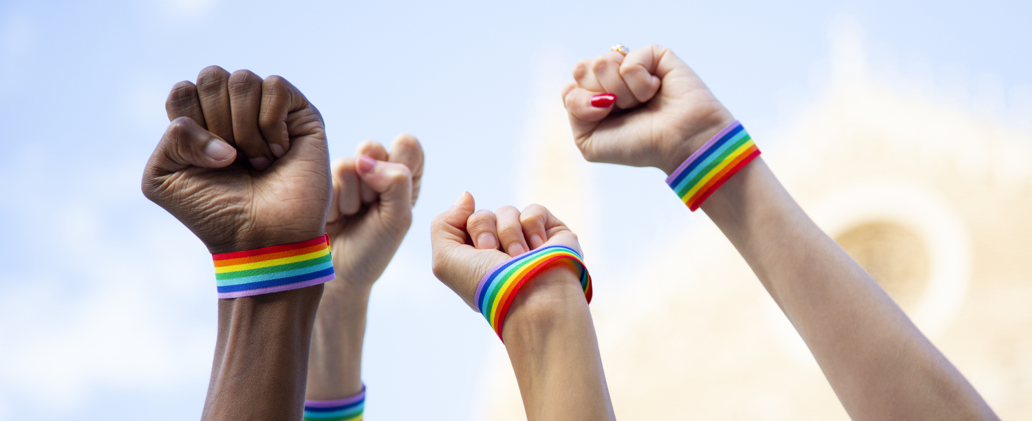 Vier vuisten in de lucht met regenboogarmbandjes