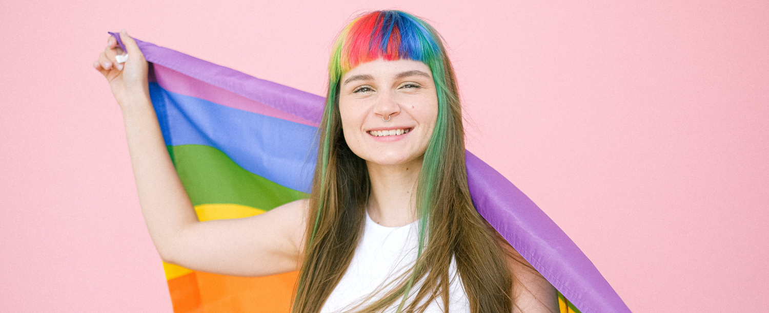 LGBTI+ jongere Persoon met regenbooghaar en regenboogvlag en roze achtergrond